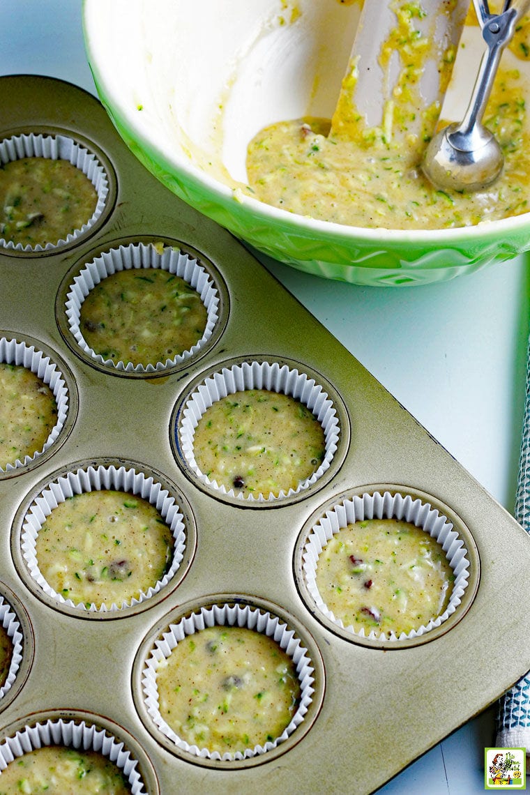 Zucchini muffins batter in a muffin tin and batter mixing bowl.