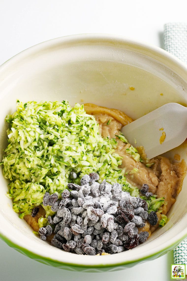 Shredded zucchini, raisins and muffin batter in a bowl with spatula.