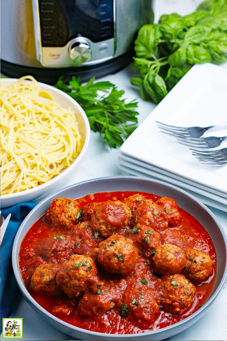 A bowl of pressure cooker meatballs in sauce with pasta, napkins, dishes and forks.