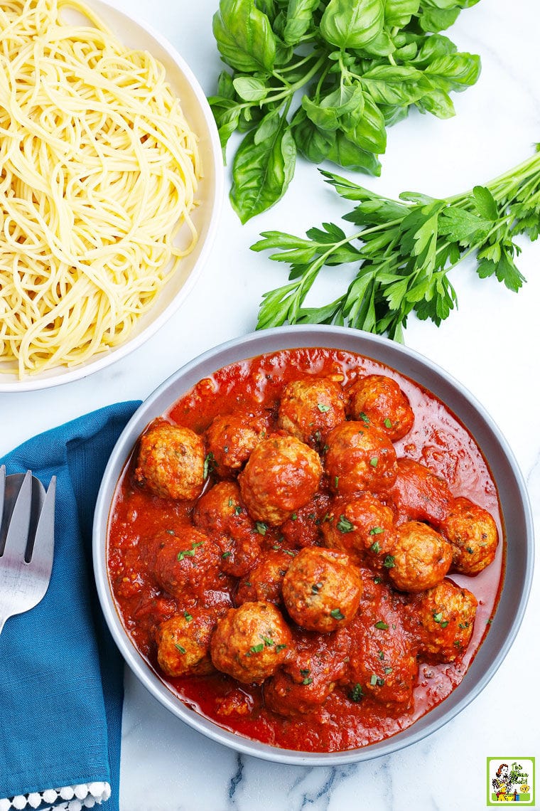 A bowl of Instant Pot Meatballs with spaghetti, parsley, basil, serving spoon and fork, and napkin.