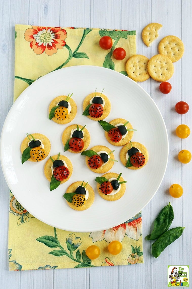 Caprese Ladybugs Appetizers on a white plate with crackers, tomatoes and basil with a floral napkin.