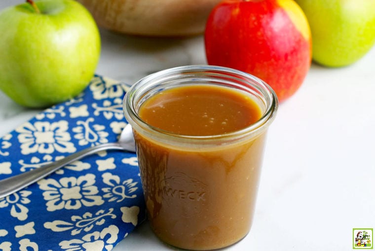 Vegan caramel sauce in a glass jar with a spoon, napkin, and apples.