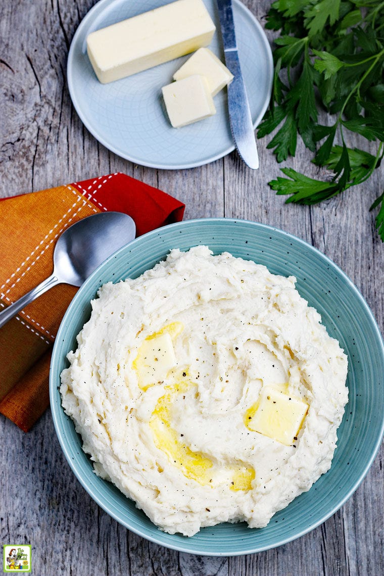 A blue plate of mashed potatoes and butter with spoon and napkin.