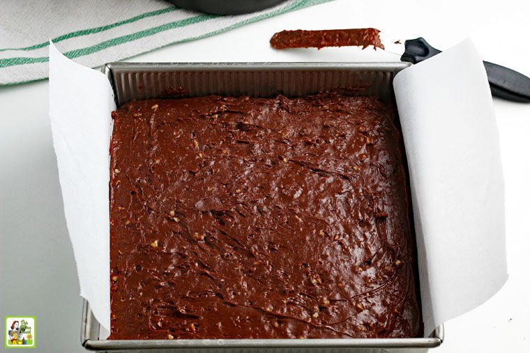 Lining a fudge pan with parchment paper with an offset spatula covered in chocolate.