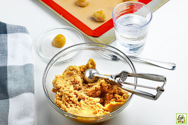 Scooping out peanut butter cookie dough with an ice cream scoop from a glass bowl.