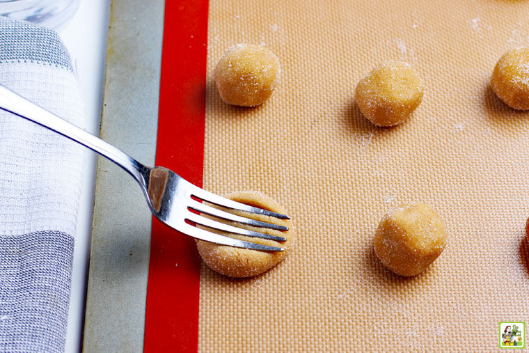 Flattening the cookie dough balls with a fork to make a criss-cross pattern.