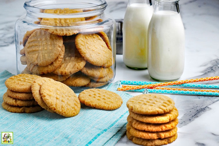 Stacks and a glass jar of Gluten Free Peanut Butter Cookies with jars of milk and colorful paper straws.