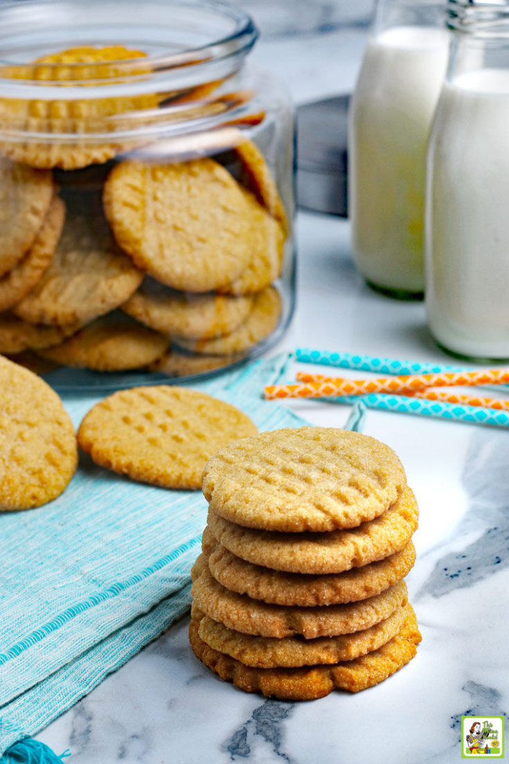 Stacks of peanut butter cookies with a glass jar of cookies and jars of milk.