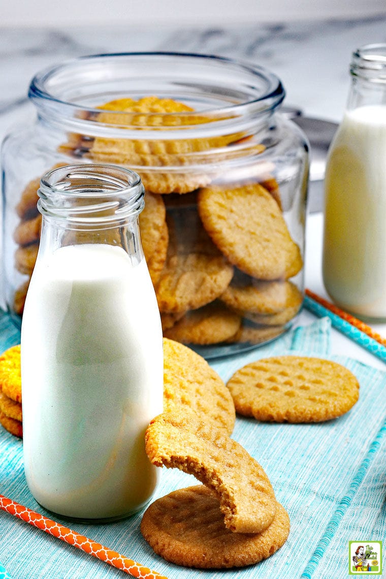 Peanut butter cookies with pint bottles of milk and a glass jar of cookies in the background.