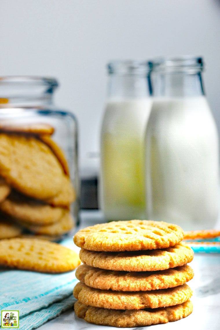 A stack of cookies with bottles of milk and a jar of cookies in the background.
