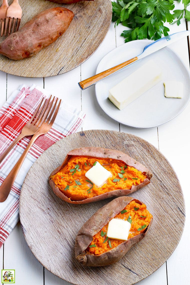 Cooked sweet potatoes with butter on a brown plate with forks, a red napkin, and a white plate with a stick of butter. 