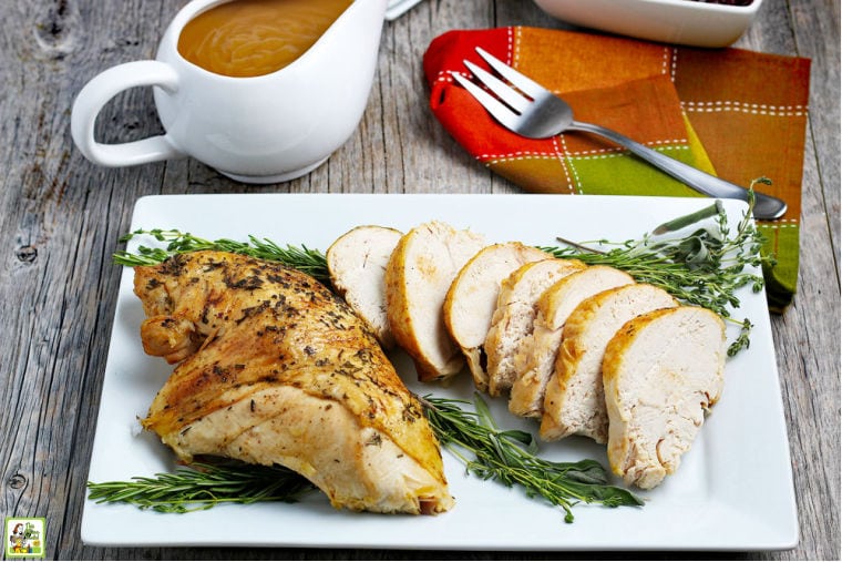 Sliced Instant Pot Turkey Breast on a white platter with herbs, napkin, fork, and a gravy boat.