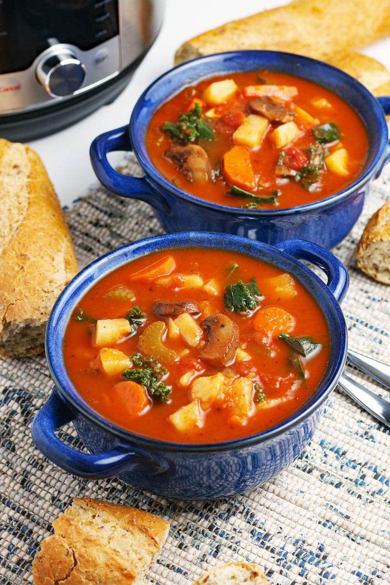 Blue bowls of vegetable soup, French bread, spoons, and a pressure cooker on a blue and white placemat. 