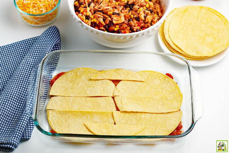 Corn tortillas layed on the bottom of a prepared baking dish.