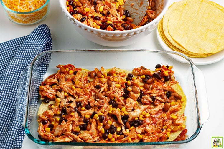 Layer of beans and chicken mixture on top of corn tortillas in a glass baking dish.