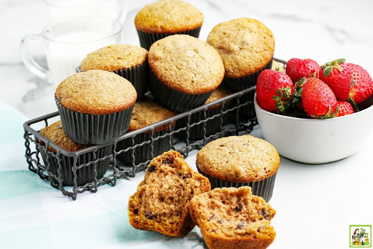 Gluten free applesauce muffins on a tabletop and in a wire basket with a bowl of strawberries.
