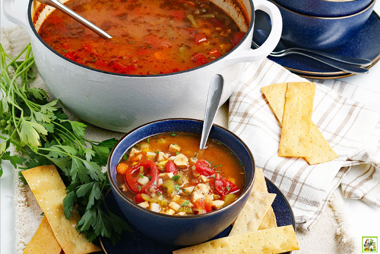 Bowls and a large pot of Chicken Vegetable Soup with crackers, fresh herbs, spoons, and napkins.