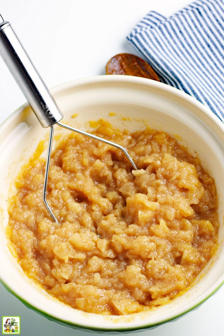 Processing a bowl of cooked apples into applesauce with a potato masher.