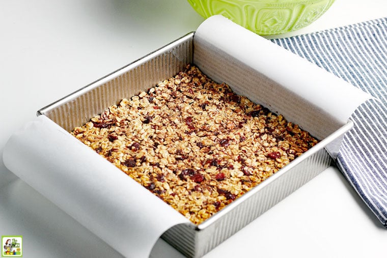 Baking homemade granola bars in a square pan with parchment paper hanging over the sides.