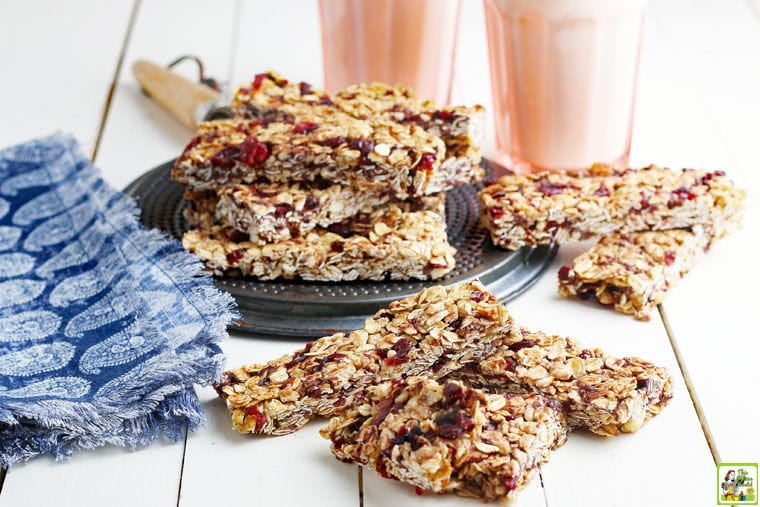 Piles of Homemade Granola Bars with a blue and white napkin and glasses of milk.