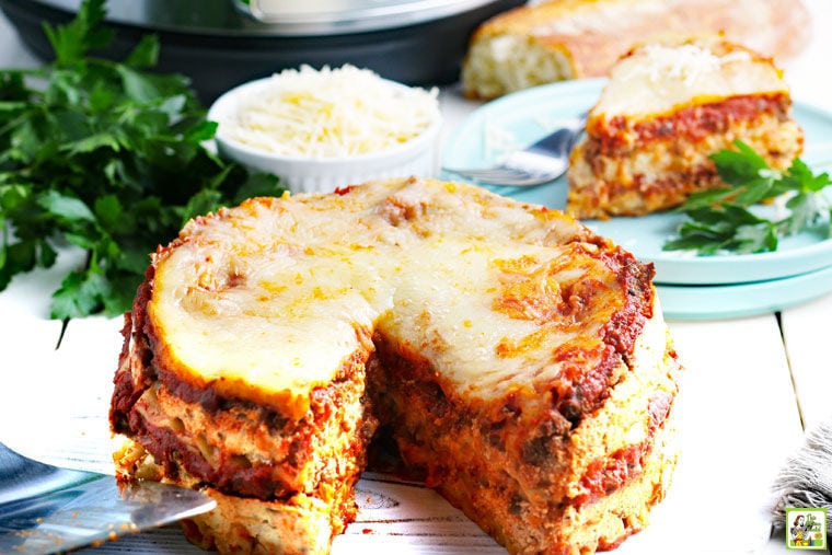 Instant Pot Lasagna with a slice cut out, with bowl of shredded cheese and a plate of lasagna in the background.