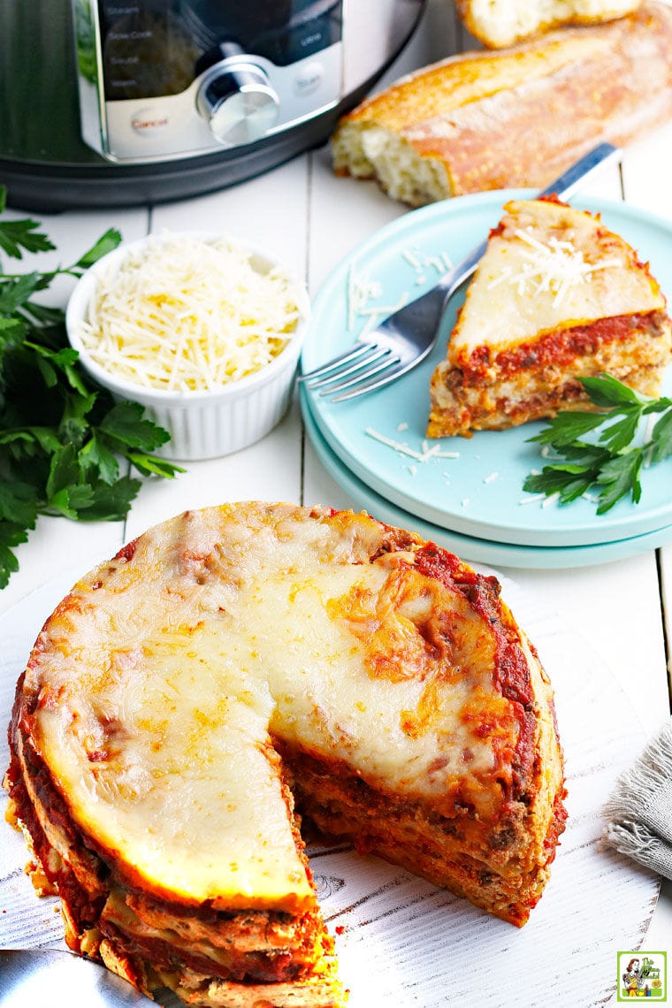 Overhead shot of pressure cooker lasagna with a slice cut removed and served on a blue plate with a fork next to a bowl of shredded cheese with fresh herbs.