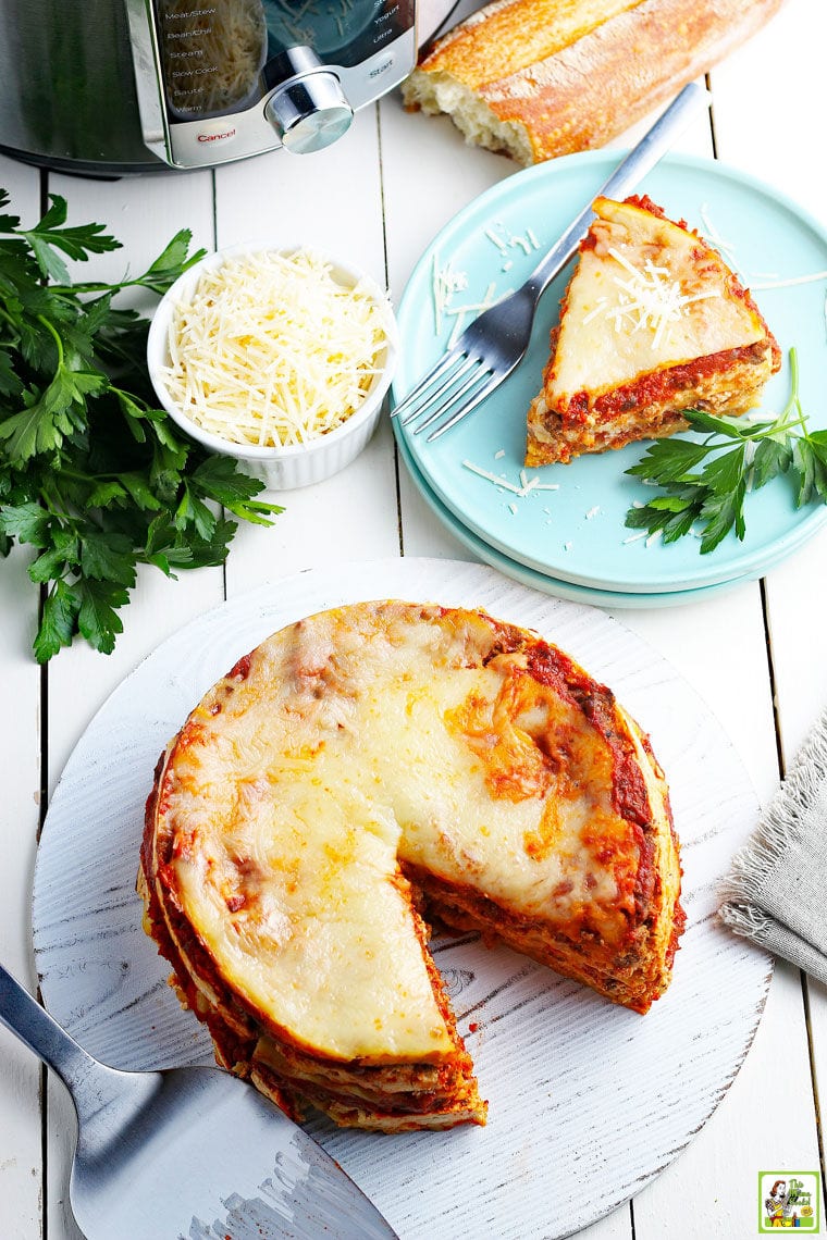 Overhead shot of Instant Pot Lasagna with a slice cut removed and served on a blue plate with a fork with fresh herbs and a bowl of shredded Parmesan. 