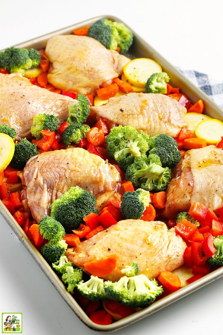 Marinated chicken skin on thighs and colorful chopped vegetables on a rimmed baking sheet.