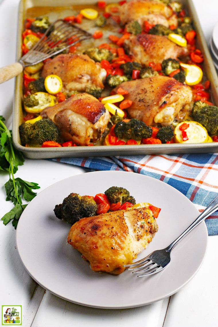 A plate of cooked chicken and vegetables with fork and napkin with a pan of baked chicken thighs and vegetables in the background.