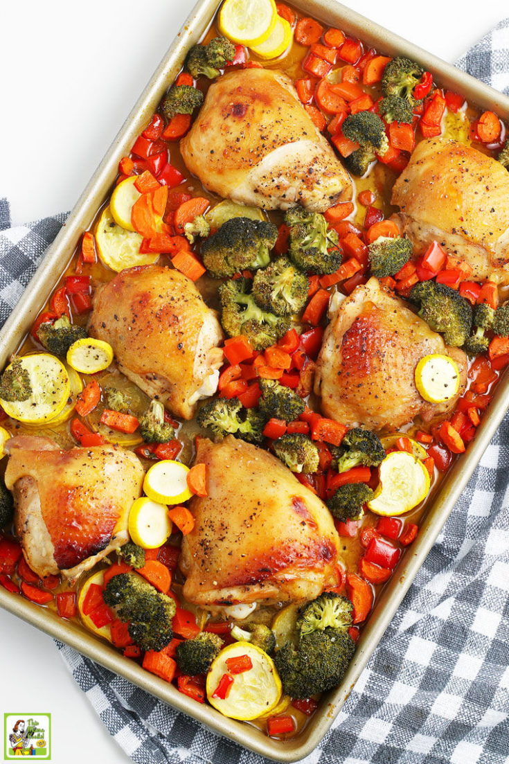 Overhead shot of roasted chicken thighs and chopped vegetables on a gray and white dish towel.