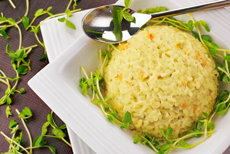A bowl of Seafood Risotto with spoon and pea shoots.