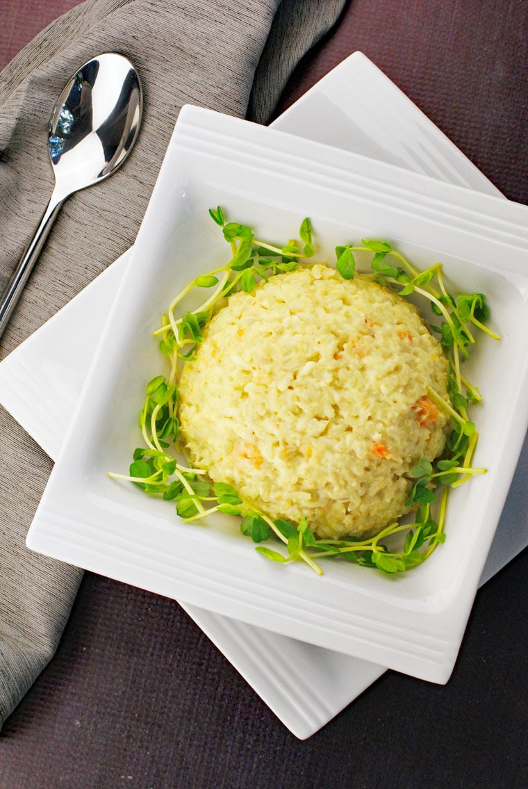 A scoop of seafood risotto in a white bowl on a plate with a silver spoon and gray napkin.