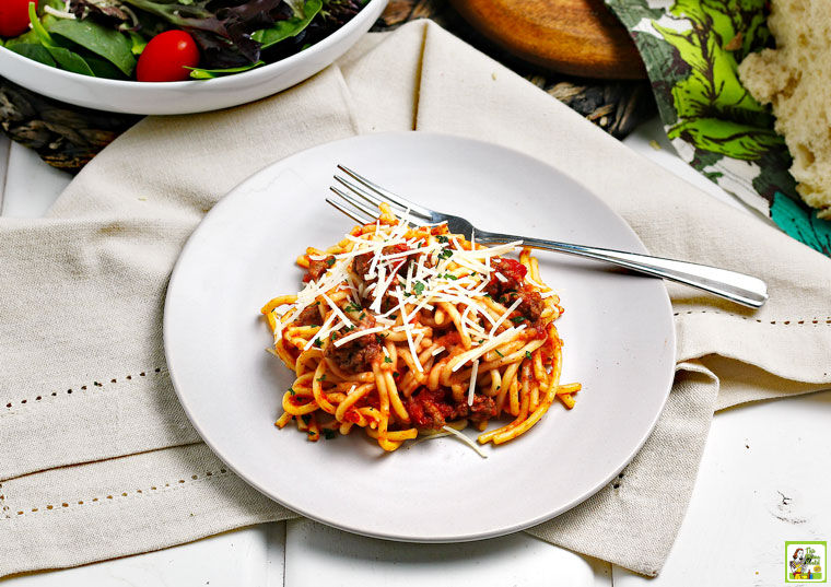 A plate of Instant Pot Spaghetti with cheese on a linen napkin with a bowl of salad.