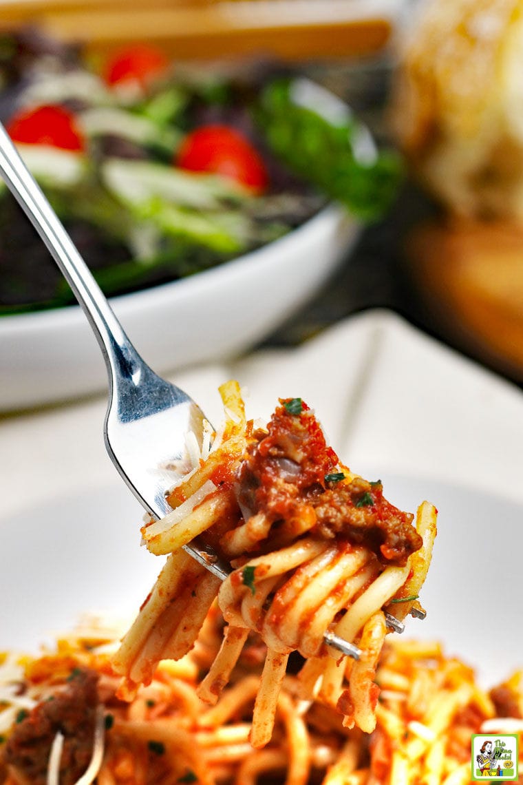 Closeup of spaghetti with meatsauce twirled around a fork with salad in a white bowl in the background.