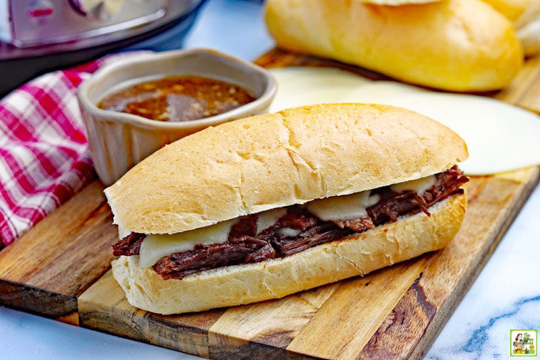 Instant Pot French Dip Sandwich with a bowl of au jus on a wooden cutting board with a napkin.