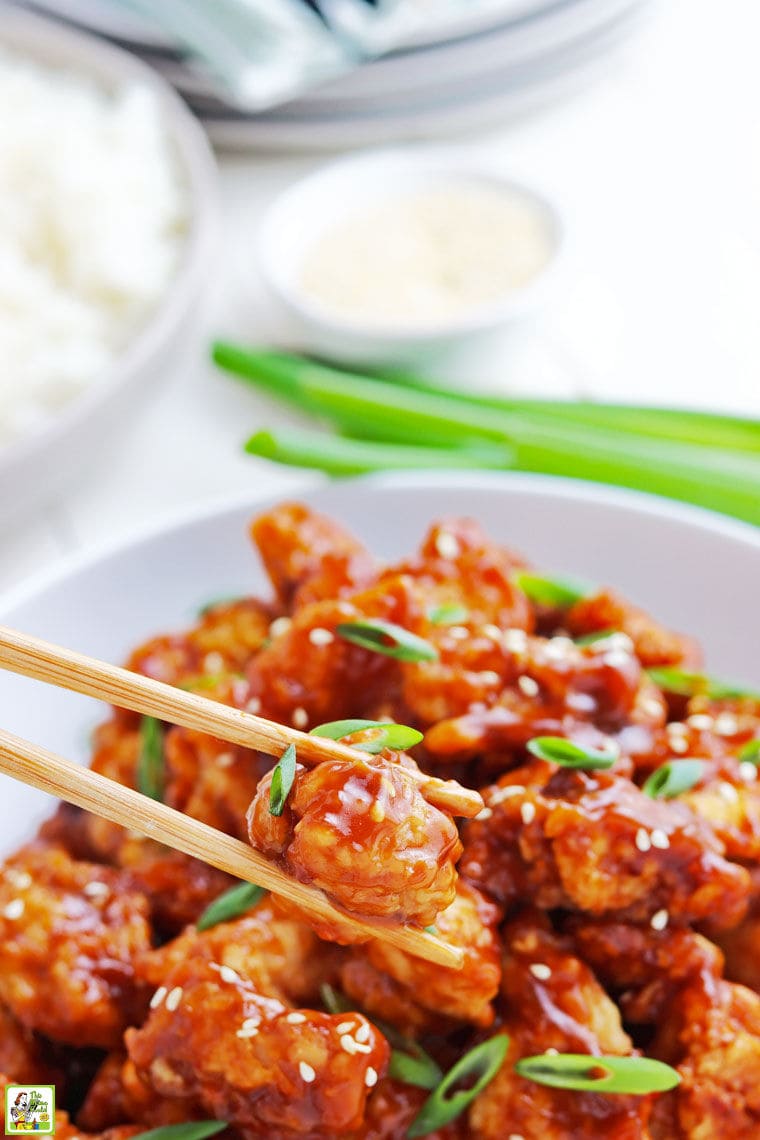 Close up of a piece of gluten free General Tso chicken being picked up out of a bowl with chopsticks.
