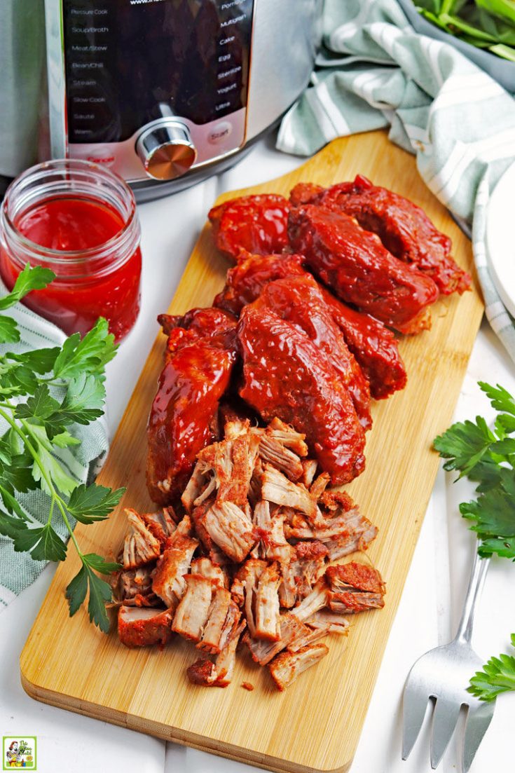 Instant Pot barbecue country style ribs wooden cutting board, a jar of BBQ sauce, and a serving fork.