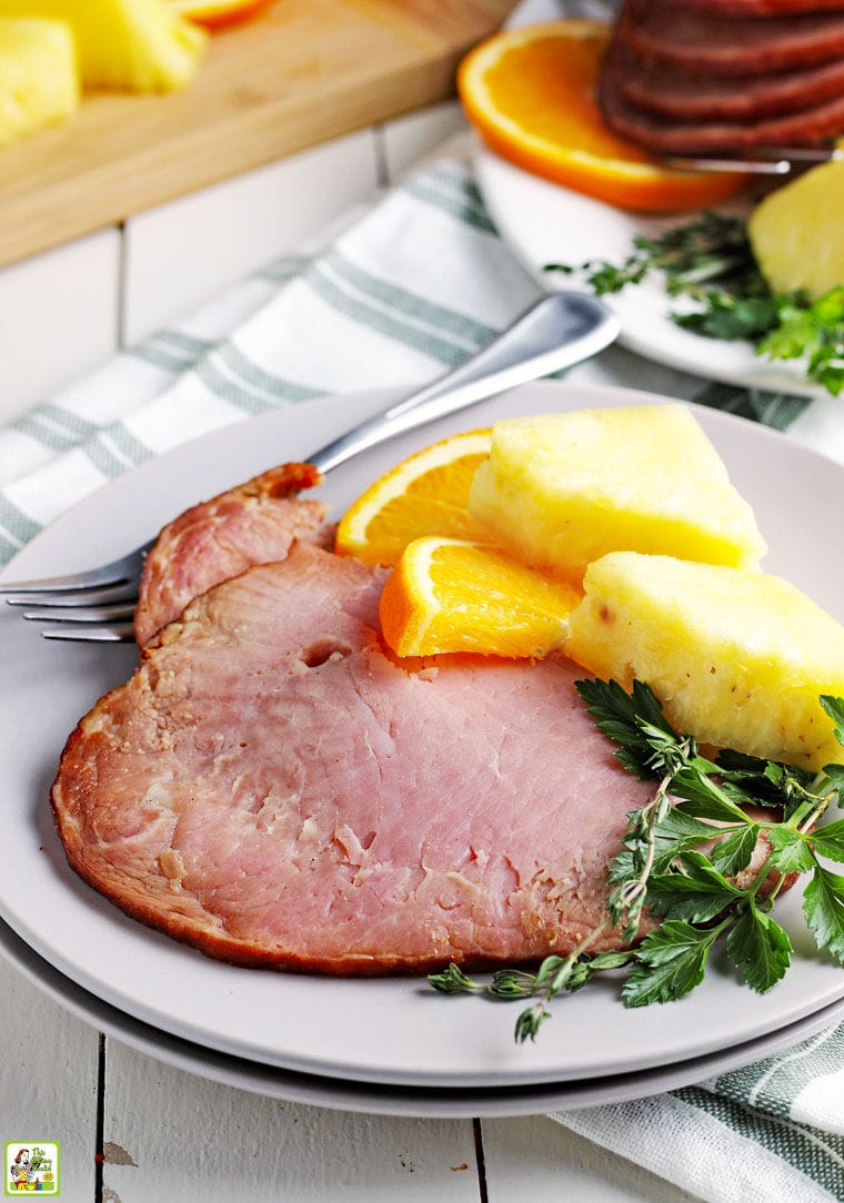 A slice of Instant Pot ham with orange and pineapple slices and herbs and a fork and napkin.