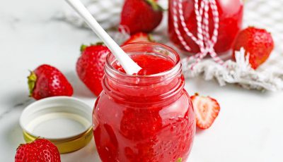 Jars of Keto Strawberry Sauce with a serving spoon and strawberries.