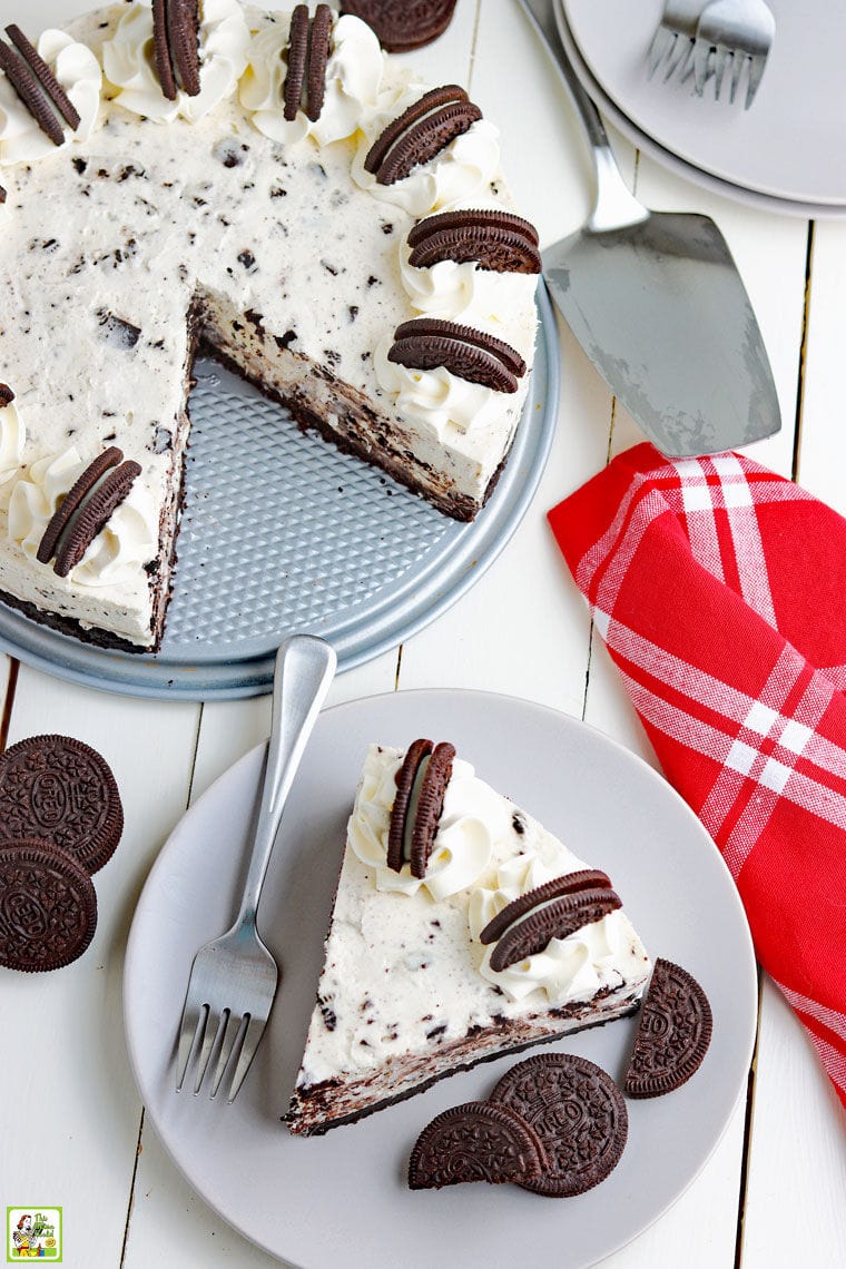 Overhead shot of a slice Oreo cheesecake on a plate with a Oreo cheesecake with a slice missing next to a cake server and a red cloth napkin.