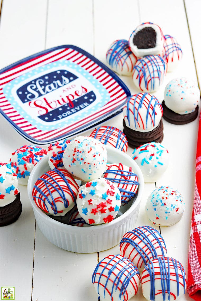 Red, white and blue dessert Oreo truffle balls in a white bowl with a Fourth of July paper plate with a red cloth napkin.