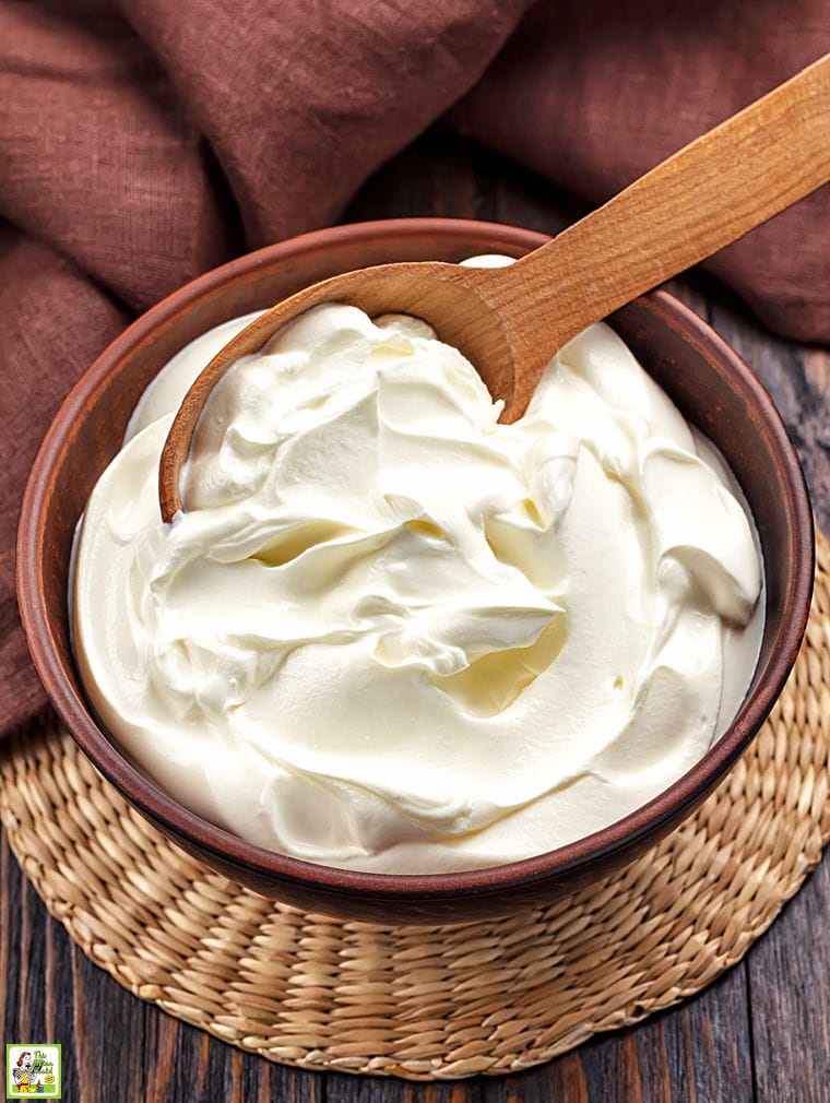 A brown bowl of sour cream with a wooden spoon and brown napkin.