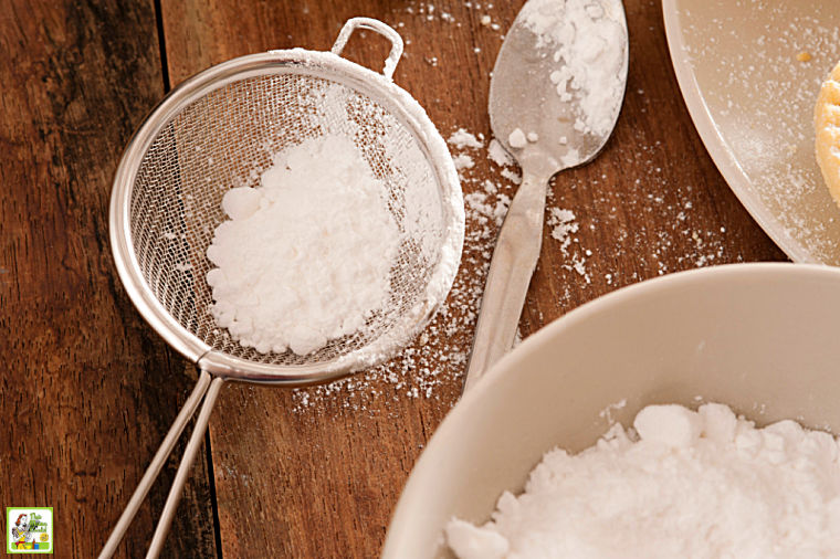 Fine mesh sieve, spoon and bowl filled with powdered sugar.