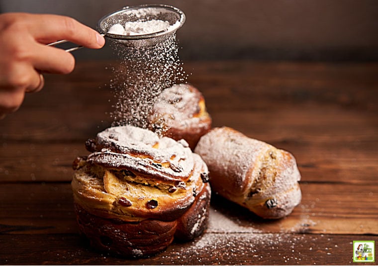 Hand sprinkling powdered sugar with a tea strainer over baked goods and pastries.