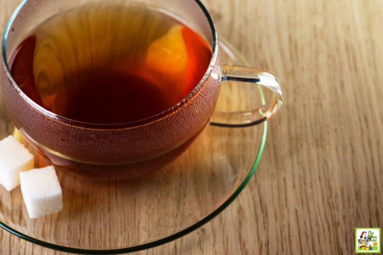 Glass tea cup and saucer with sugar cubes on a wooden tabletop.