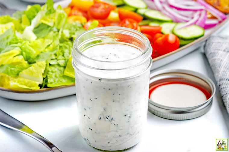 A mason jar of Low-Carb Keto Ranch Dressing with a platter of salad fixings.