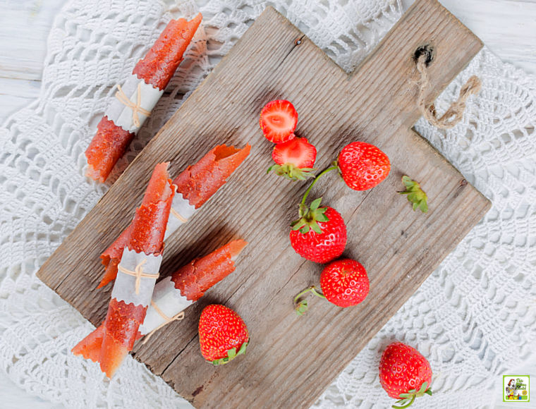 Strawberry Fruit Leather Roll-Ups on a wooden cutting board with strawberries.