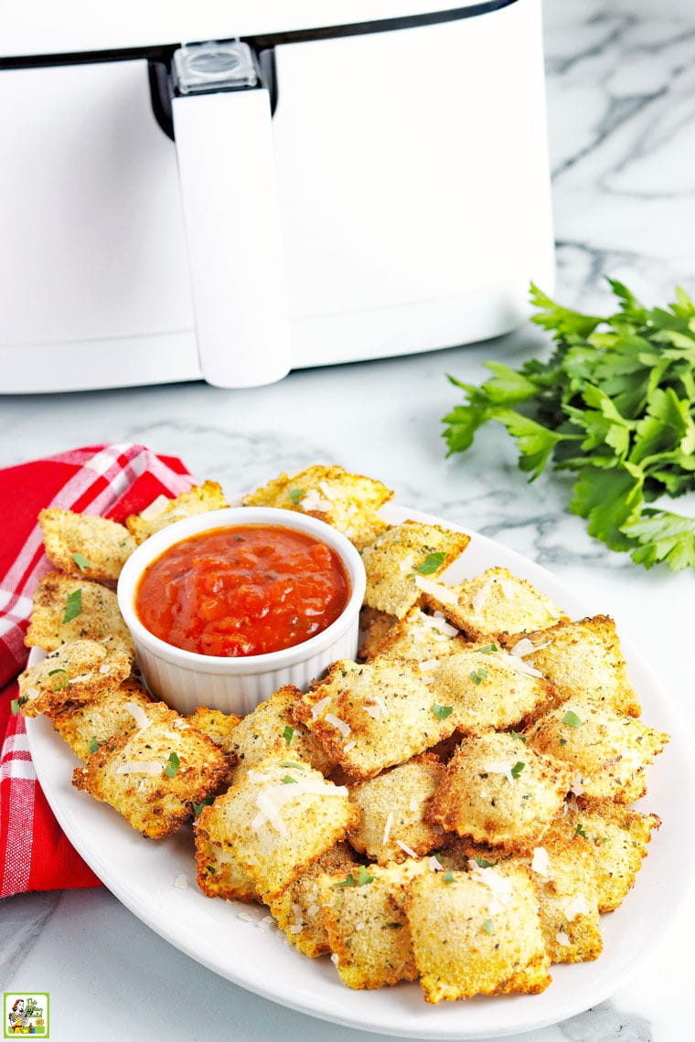 A platter of fried air fryer ravioli with dipping tomato sauce with napkin and an air fryer in the background.