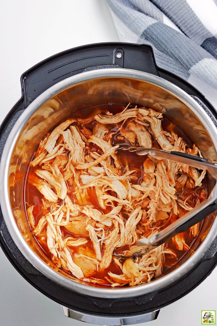 Overhead of Instant Pot Pulled BBQ Chicken with tongs in the open pressure cooker.