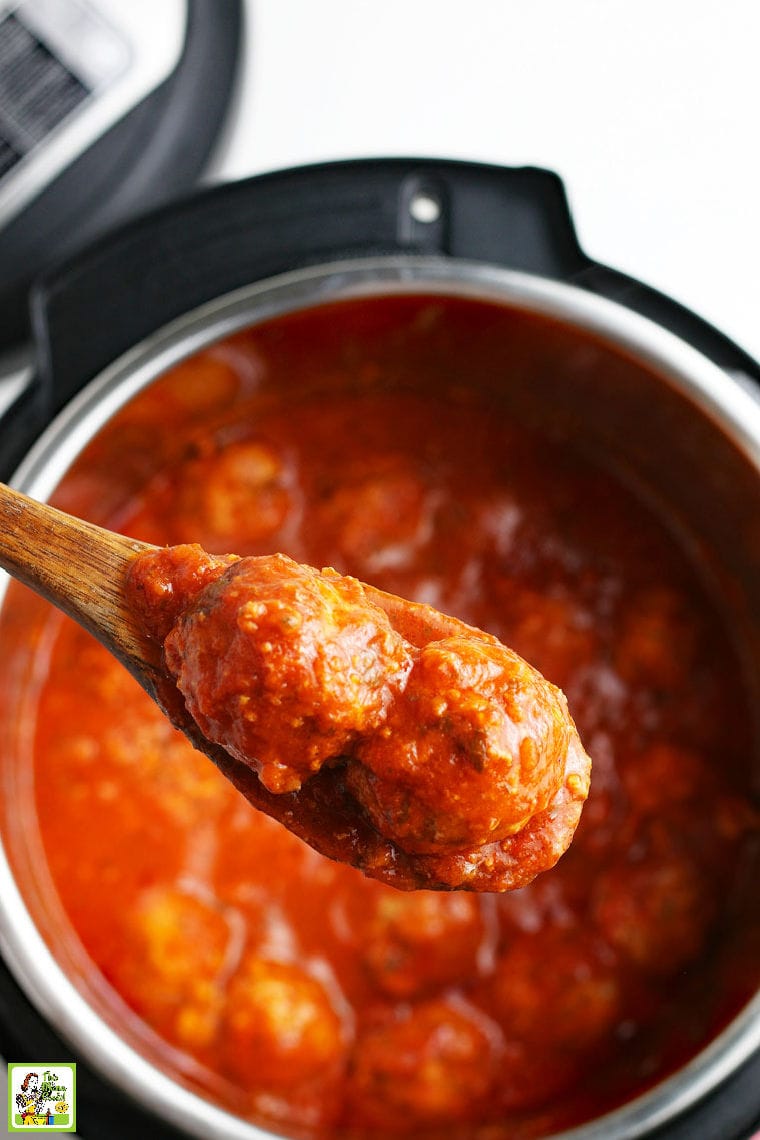 A wooden spoon with two meatballs in tomato sauce over an open Instant Pot of meatballs in sauce.